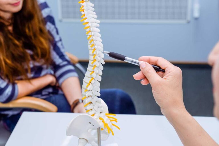 A physical therapist guides an adult through a gentle stretching exercise in a bright treatment room.
