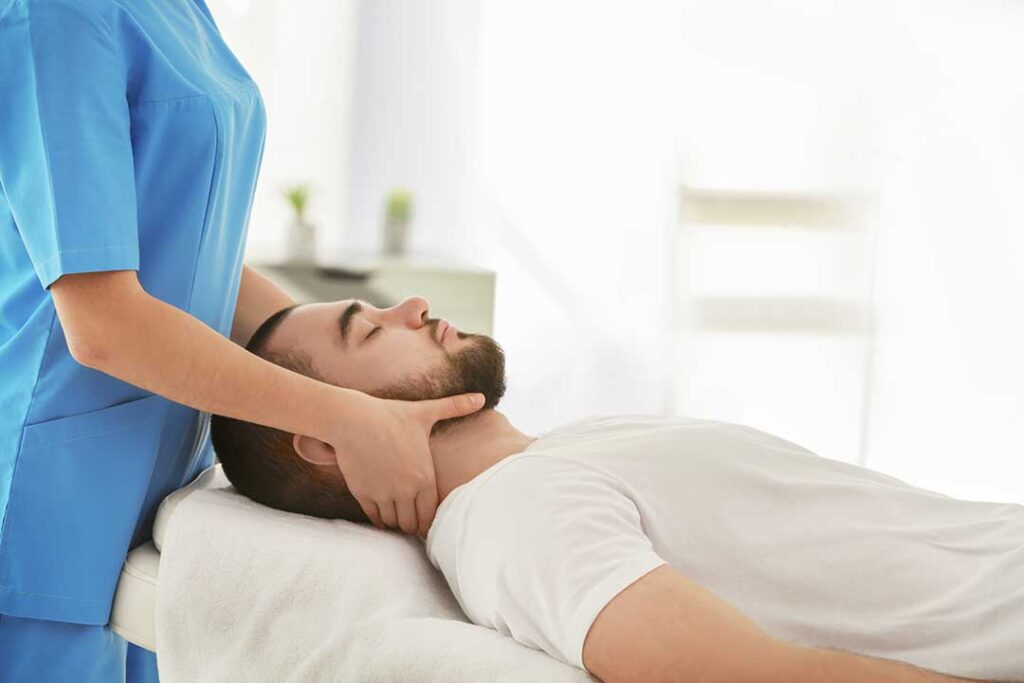 A chiropractor gently checks a patient's spine as they lie face down on a padded table.