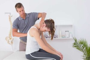 Person sitting on the edge of a bed while a clinician performs a balance and head-position assessment.